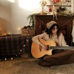 Mujer tocando guitarra junto a decoración de Navidad